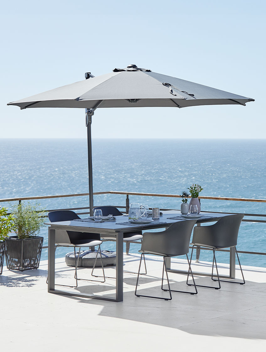 Okyanus kenarındaki verandada büyük asma şemsiye, bahçe masası ve sandalyeler